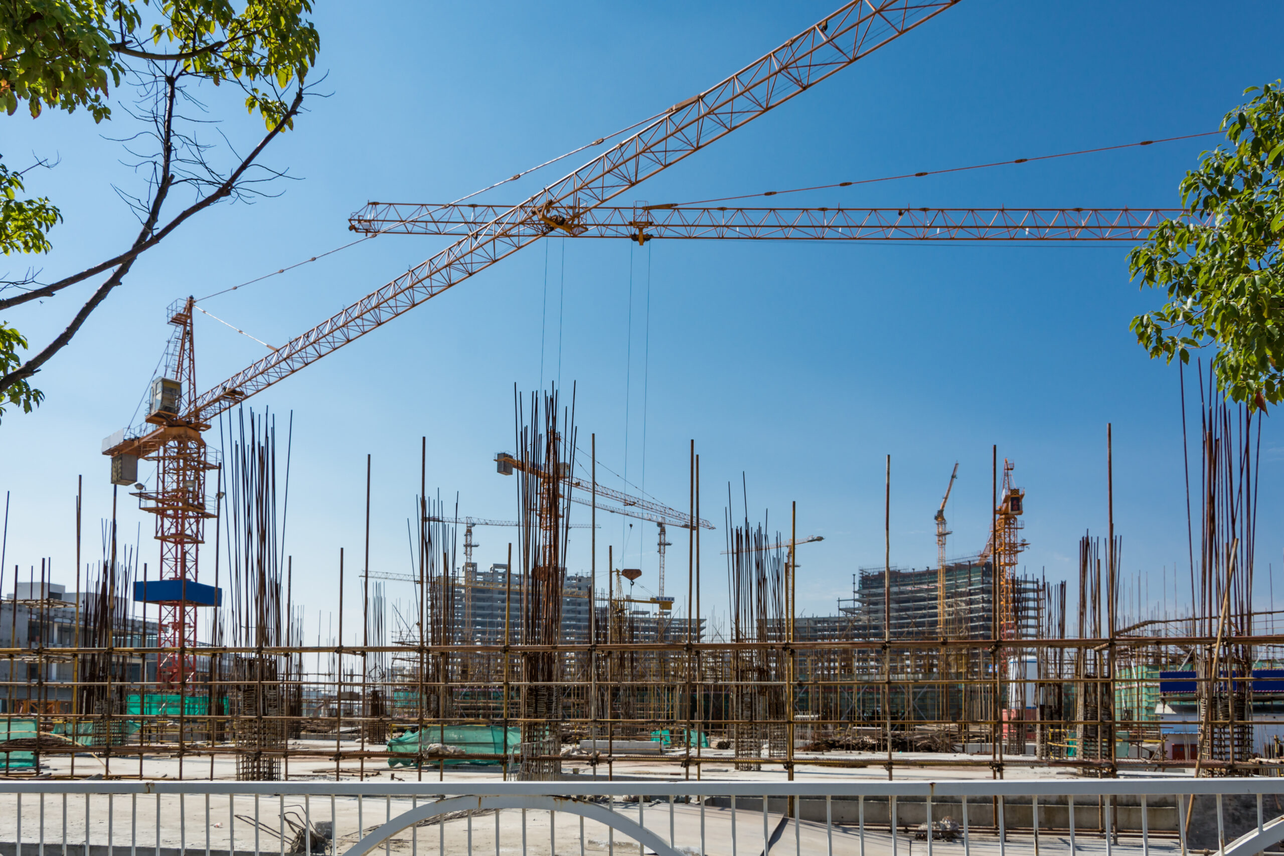 Large construction site with scaffolding building, yellow tower crane and clear blue sky.